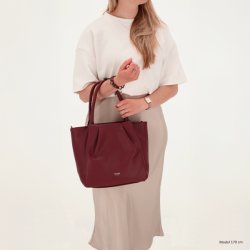 Kvinde i lys nederdel med Charm London Lyon shopper i bordeaux b�ret i de lange hanke foran kroppen.