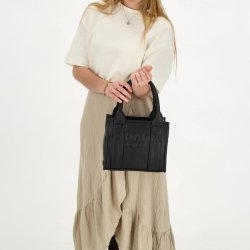 Kvinde i lys bluse og beige nederdel med Charm London Bond sort h�ndtaske b�ret i de korte hanke.